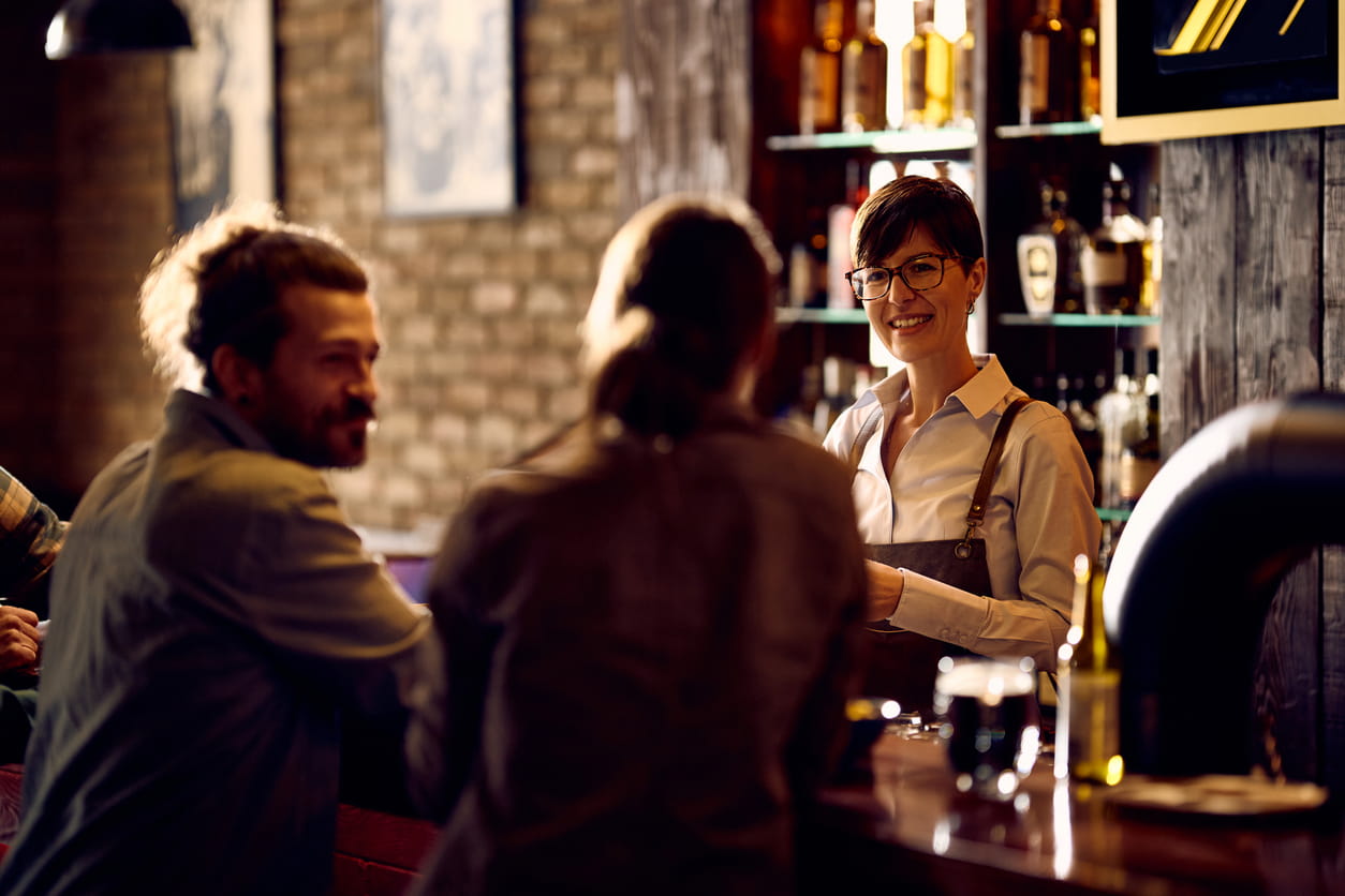 mujer trabaja en barra de bar atiendo a dos clientes