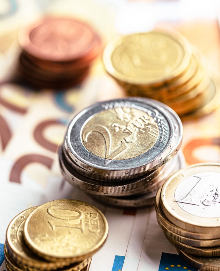 Torre de monedas sobre billetes: monedas de 10 y 20 céntimos en los extremos, monedas de 2 euros en el centro y monedas de 1 euro a la derecha.