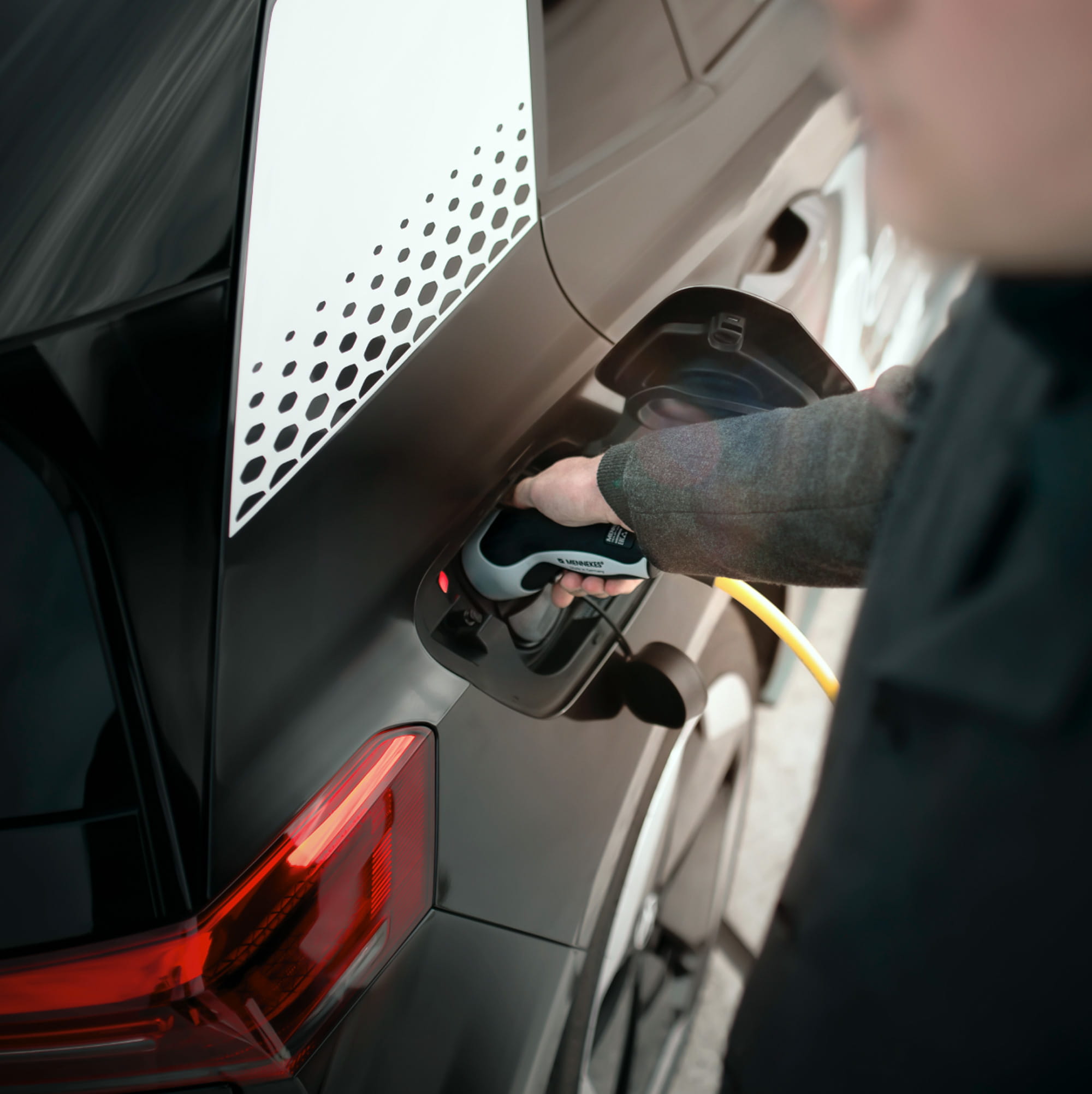 Persona a la derecha enchufando un coche eléctrico.
