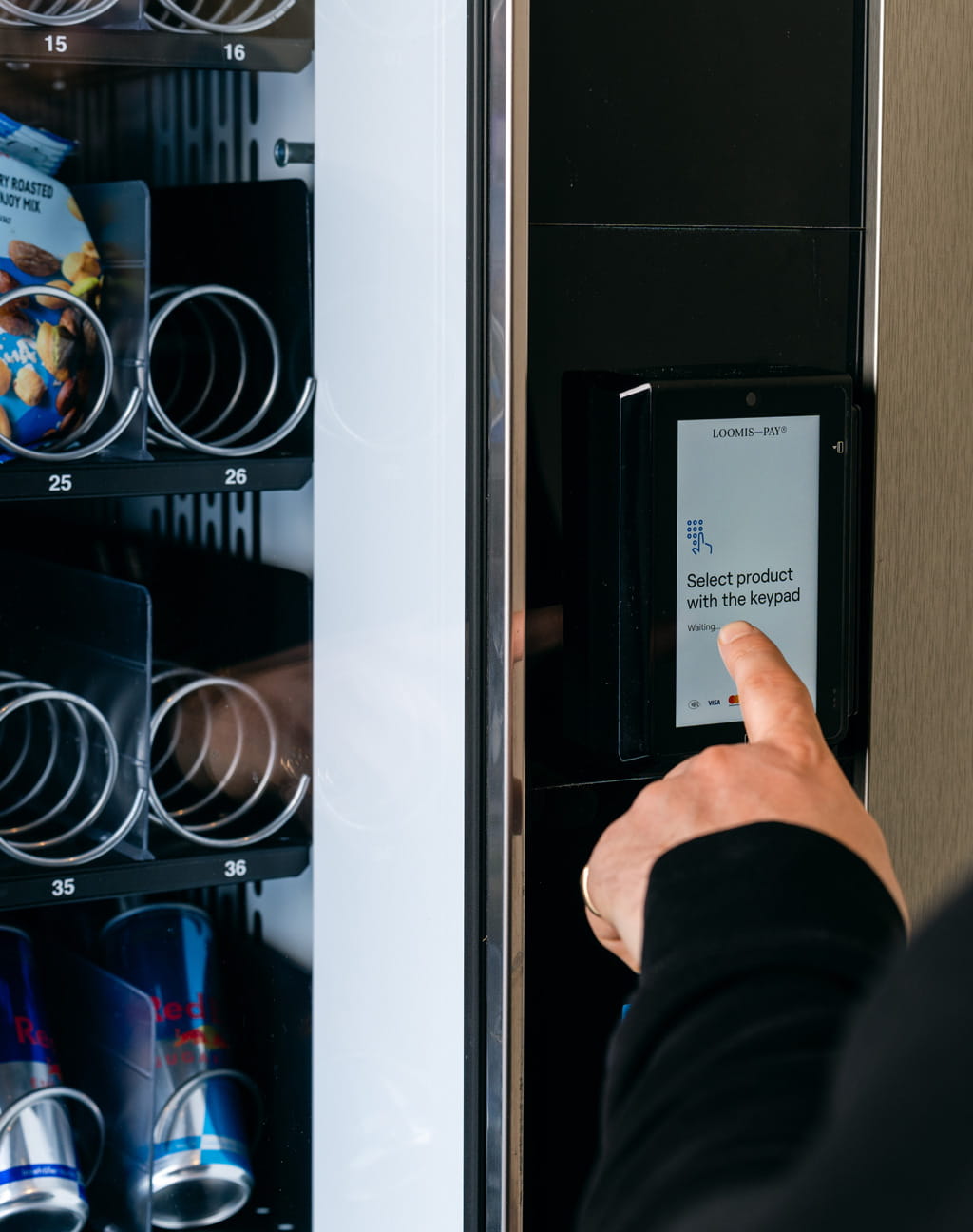 Máquina vending con el dispositivo desatendido y el dedo de una persona tocando la pantalla.