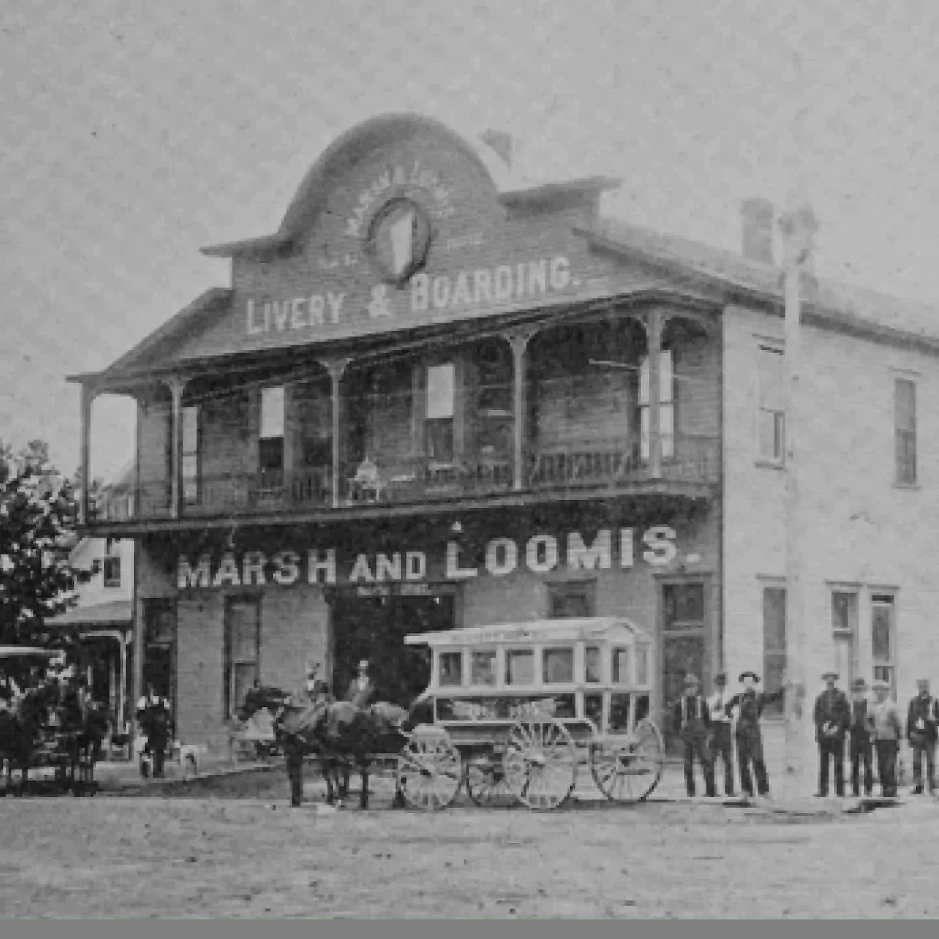 Fotografía en blanco y negro de una casa antigua con un letrero que dice "Marsh and Loomis.