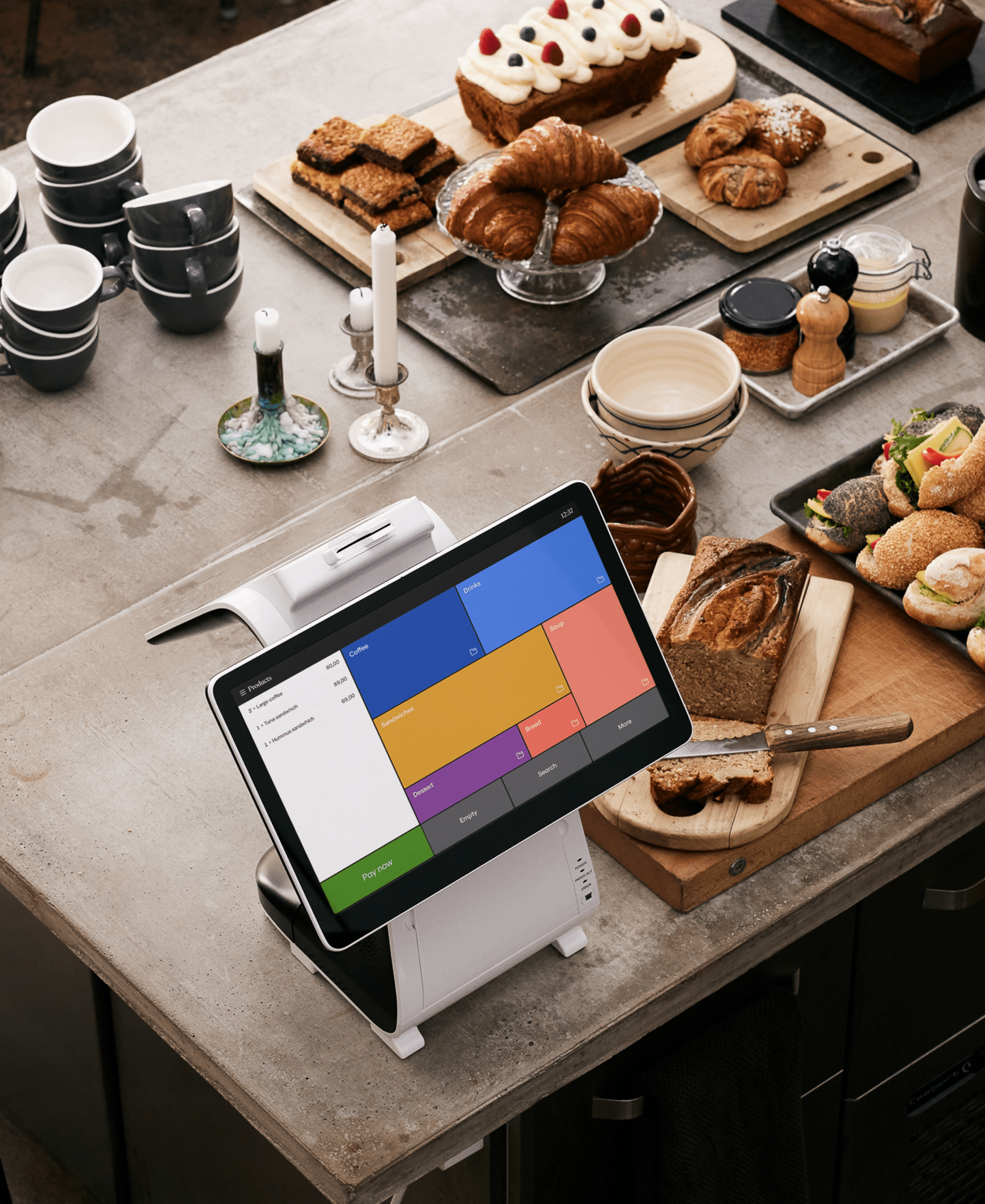 El dispositivo E800 con el software Loomis Pay sobre una mesa, con productos de panadería a la derecha y en el fondo a la derecha del dispositivo.
